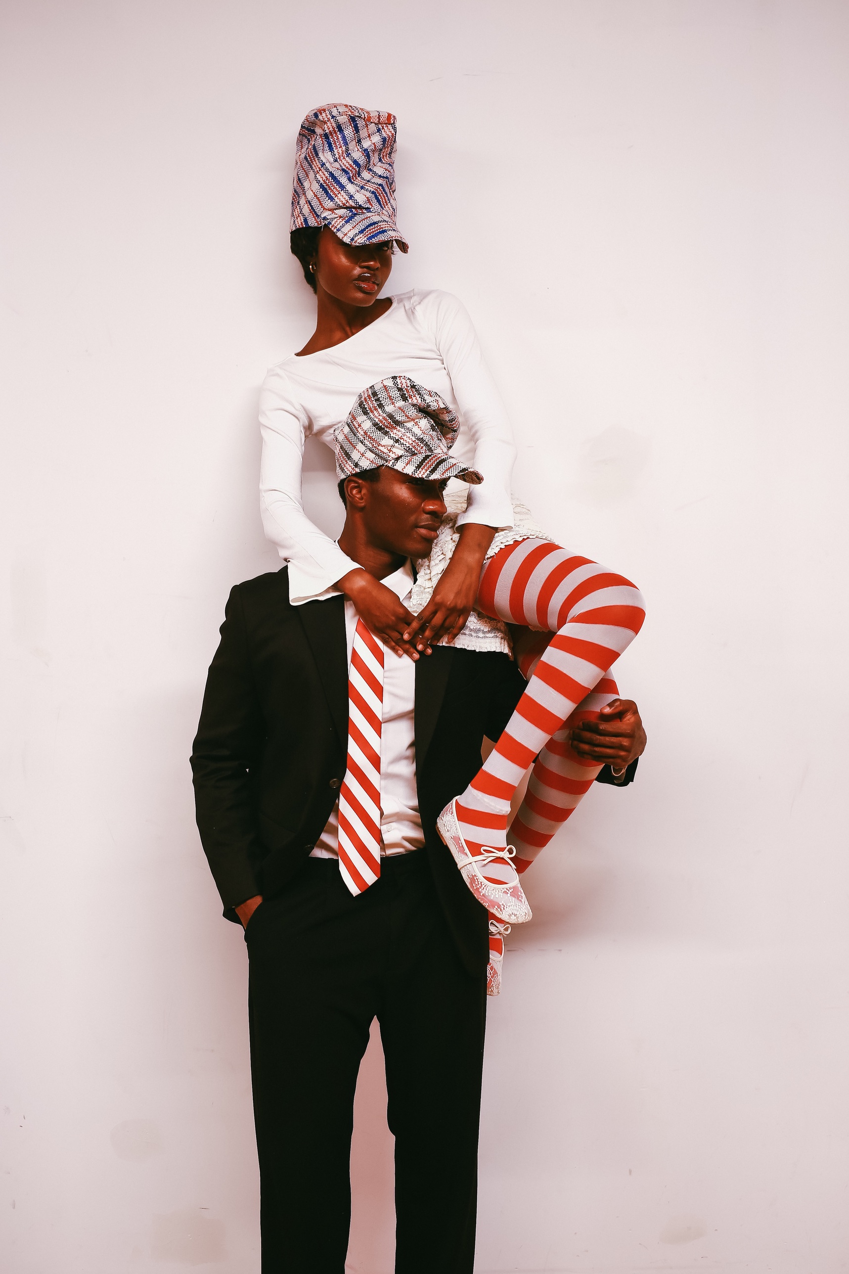 A model in a Homecoming Hat sitting on another model's shoulders against a white wall